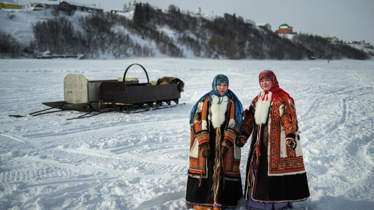 Young women from small indigenous small-numbered peoples of the North wearing traditional northern dresses pose for the camera