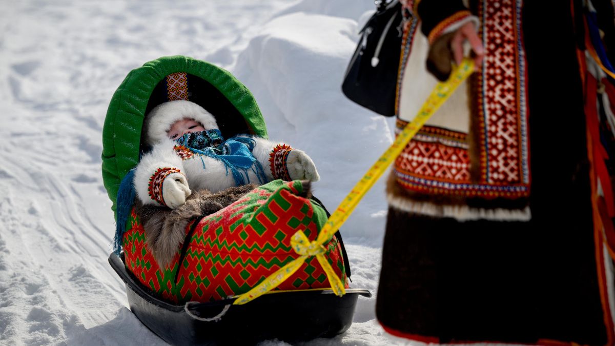 A woman carries a child in a cradle decorated with a traditional ethnic Northern ornament